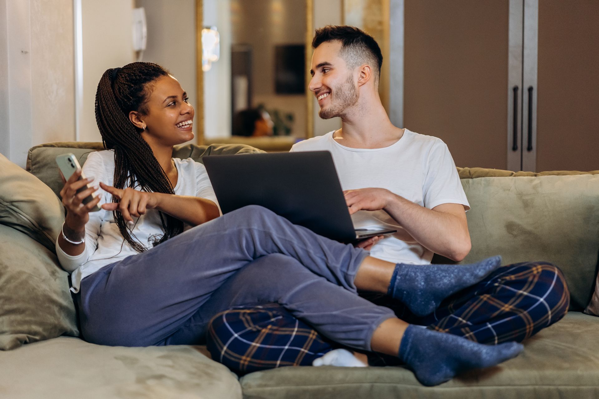 Paar entspannt auf dem Sofa und vergleicht Kreditangebote bequem per Laptop und Smartphone